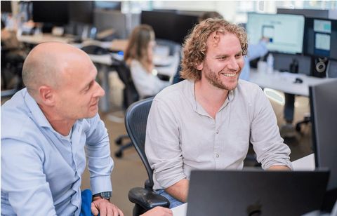 Twee collega's overleggen lachend achter een beeldscherm